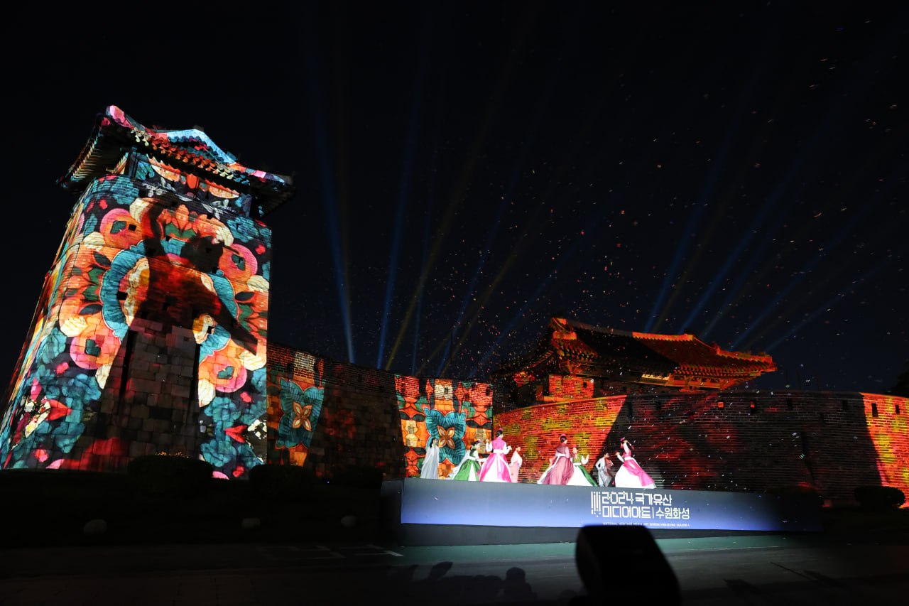 수원화성 성벽에 화려한 미디어 아트가 펼쳐지는 가운데, 무대 위에서 무용수들이 공연하고 있다.