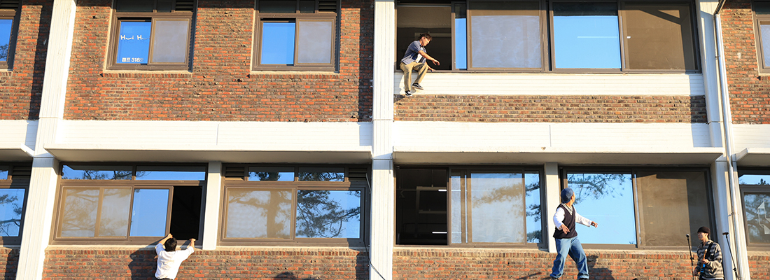 야외 광장에서 두 명의 남성 공연자가 커다란 사다리 모양의 기구에 거꾸로 매달려 곡예를 펼치고 있고, 많은 관객들이 앉아서 이를 지켜보고 있다.